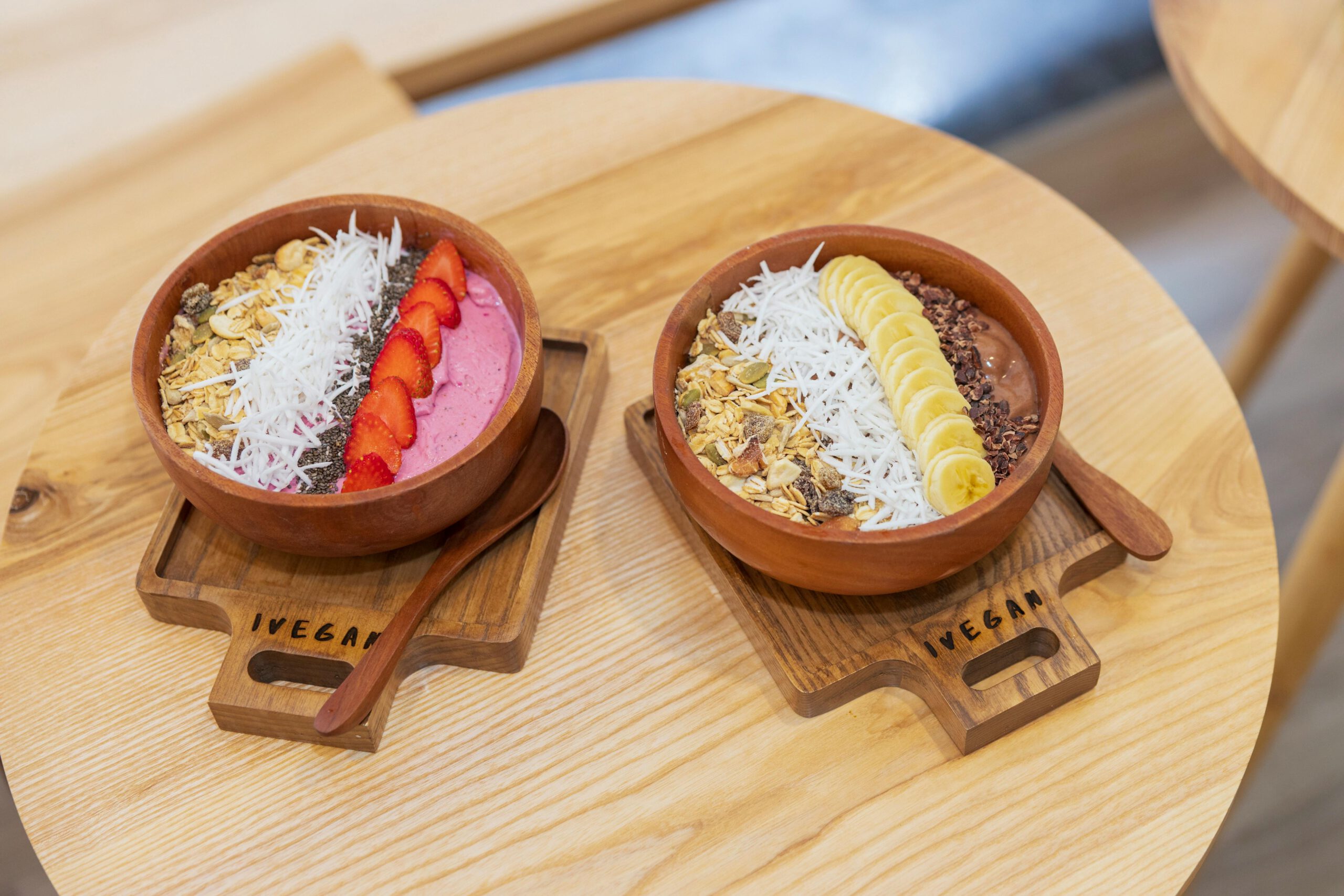 Bunte vegane Smoothie-Bowls mit Früchten und Müsli auf einem Holztisch.